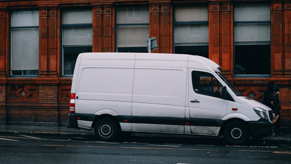 A city street in Chelsea with a mix of historic and modern buildings featuring brick, stone, and large windows, some with decorative arches. A small white van is parked on the pavement, near the entra