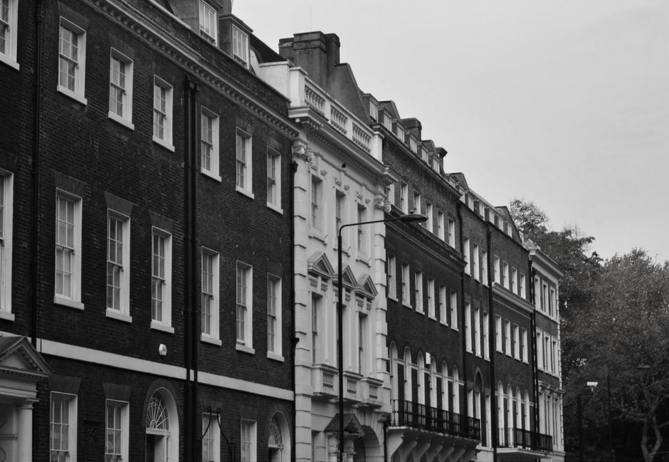 Black and white photograph of a row of Georgian-style terraced houses in Chelsea, showing multiple floors with large sash windows and decorative architectural details. The buildings are constructed wi